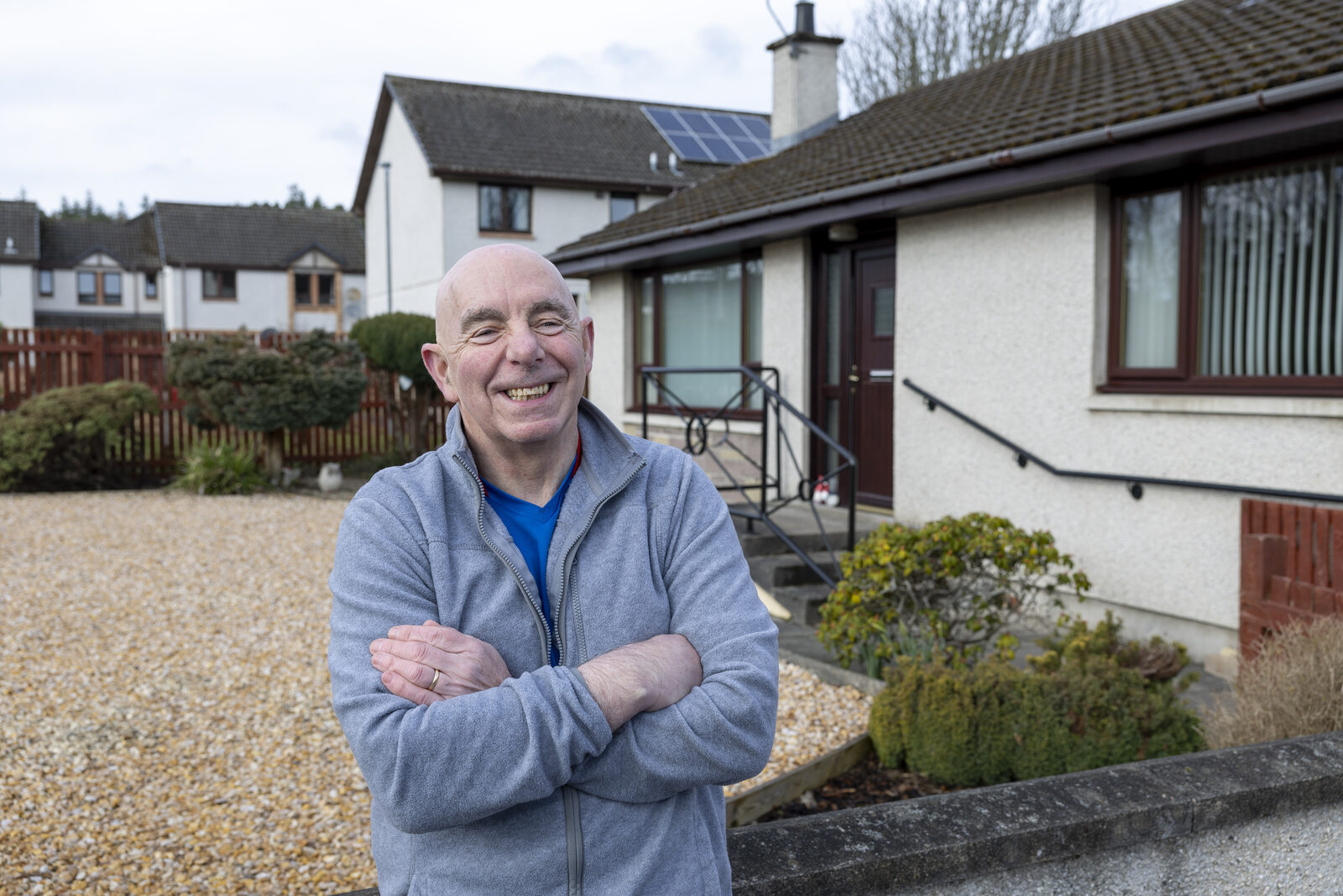 Gordon standing outside his bungalow with his arms folded, smiling