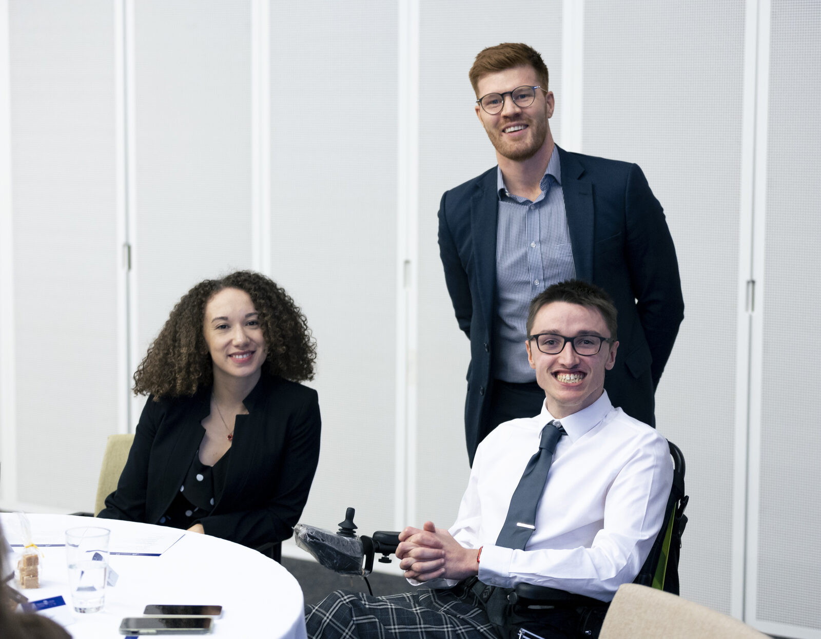 Three people smiling together at a table at a Housing Options Scotland event, one of them a wheelchair user